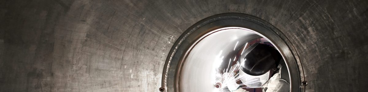 Welder or metal worker working inside a tunnel viewed down the length with receding perspective framing him as he works